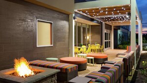 An outdoor patio with a fire feature, seating, and a covered area with string lights. - Home2 Suites by Hilton Frederick (Frederick)