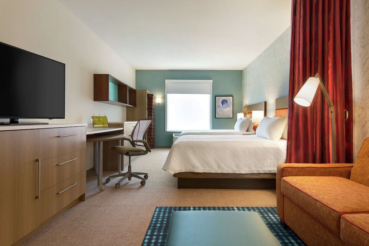 A hotel room with a bed, a desk with a chair, a television, and a window with curtains.