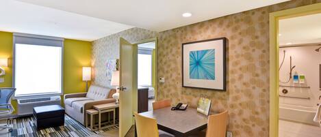 A hotel room with a bed, a desk, a chair, a lamp, a painting, and a bathroom.