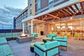 An outdoor seating area with fire pits and modern furniture, a covered patio with string lights, and a building with large windows and a brick facade. - Home2 Suites by Hilton Helena (Helena)