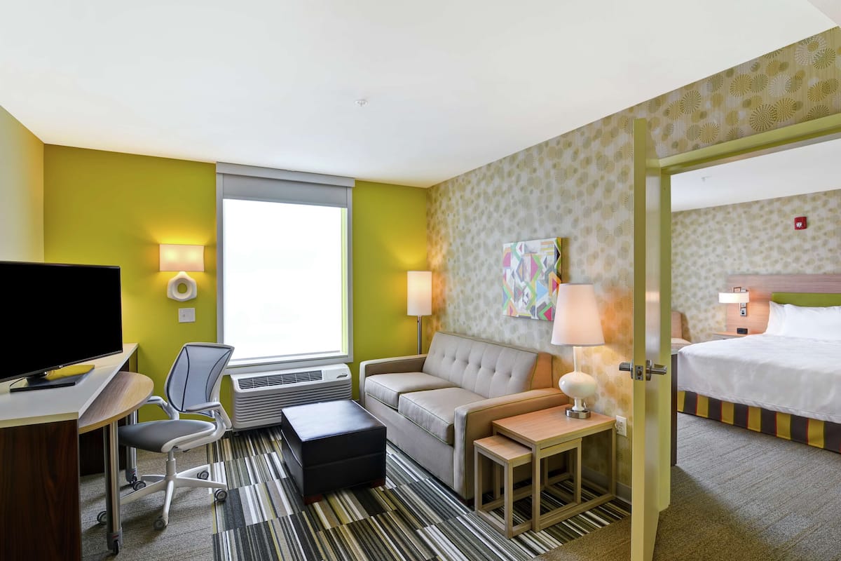 A hotel room with a bed, a sofa, a desk with a TV, a chair, a small table, and a lamp.