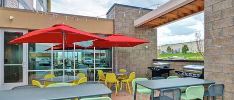 An outdoor patio area with tables and chairs, red umbrellas, and a barbecue grill.