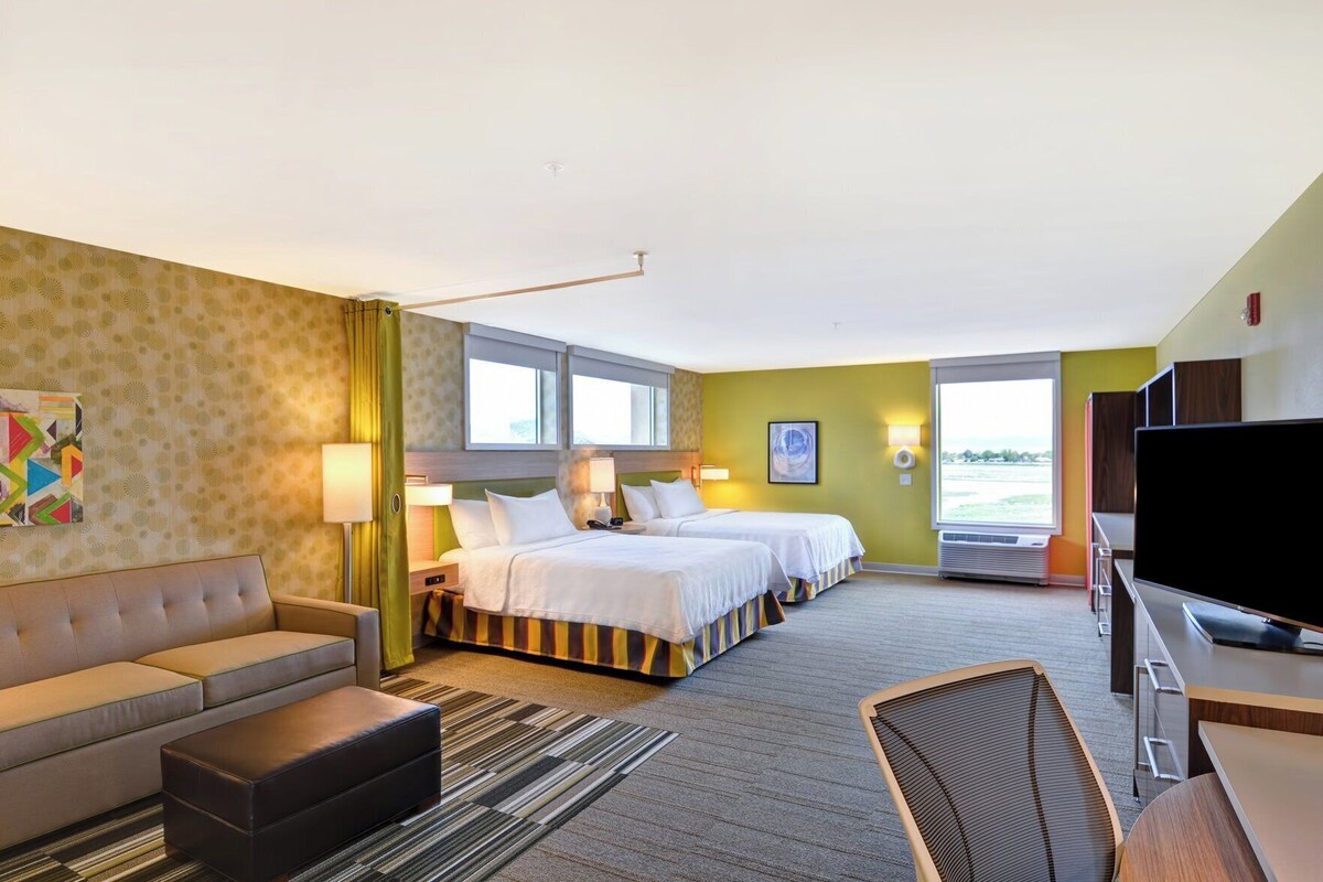 A hotel room with a sofa, two beds, a TV, and a large window.