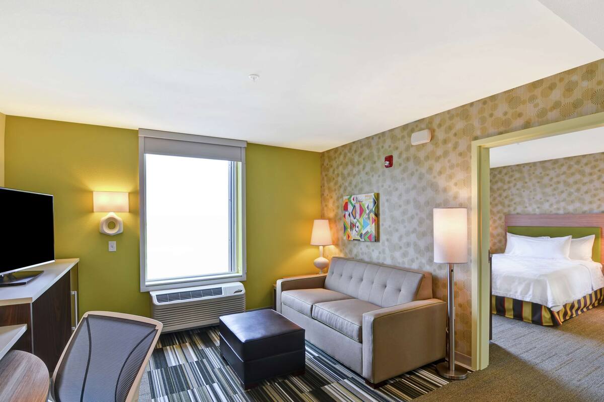 A hotel room with a sofa, a TV, a desk, a lamp, and a bed.