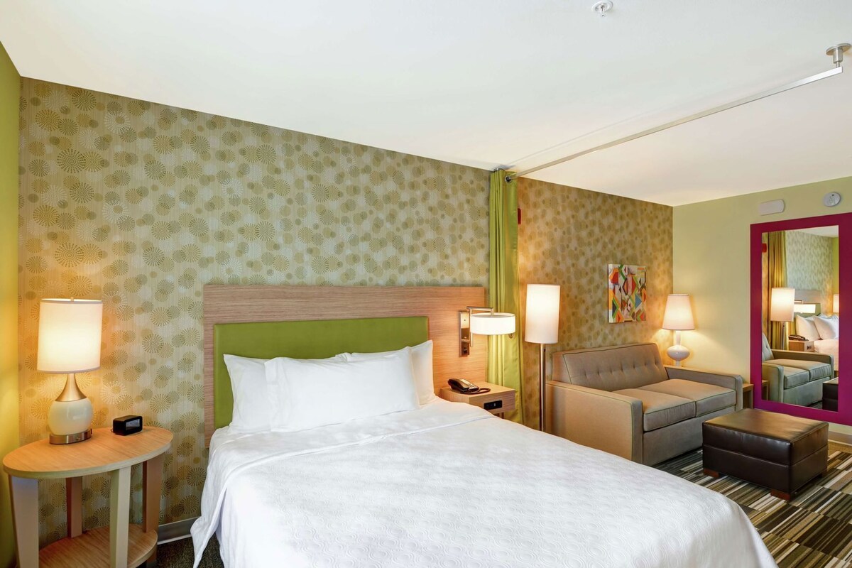 Une chambre d’hôtel avec un lit, un canapé, une table de chevet, une lampe et un miroir.