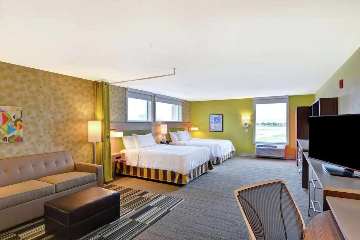 A hotel room with a sofa, two beds, a TV, and a view of the outdoors.