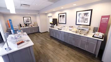 A modern kitchen area with a buffet setup, including a coffee machine, various food items, and a beverage dispenser.