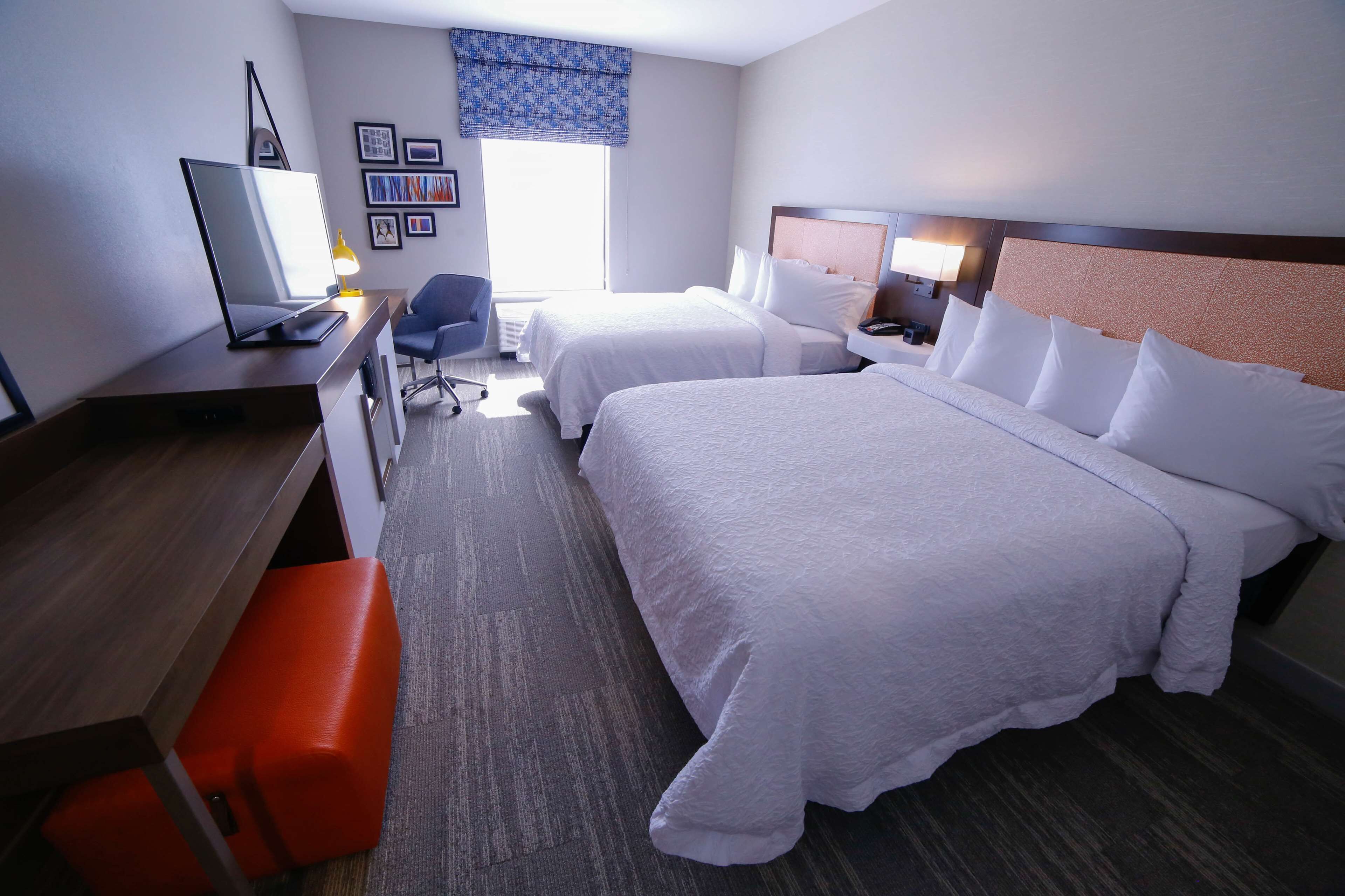 A hotel room with two beds, a desk, a chair, a TV, and a window with a view.