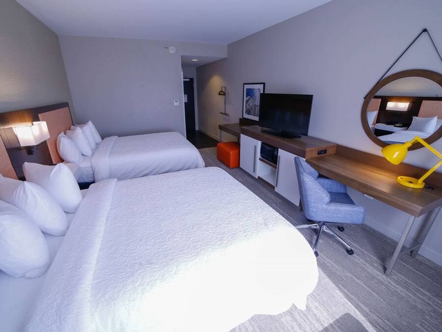 Habitación de hotel con dos camas, un escritorio, una silla, un televisor y un espejo.