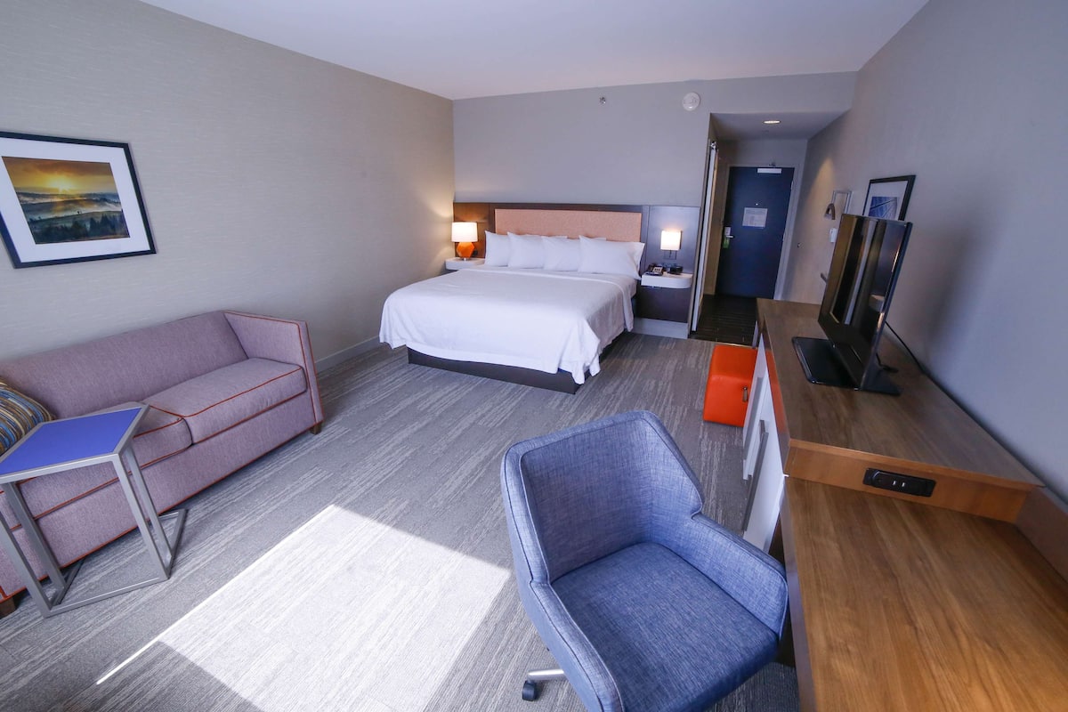 Ein Hotelzimmer mit einem Bett, einer Couch, einem Sessel, einem Schreibtisch und einem Fernseher.