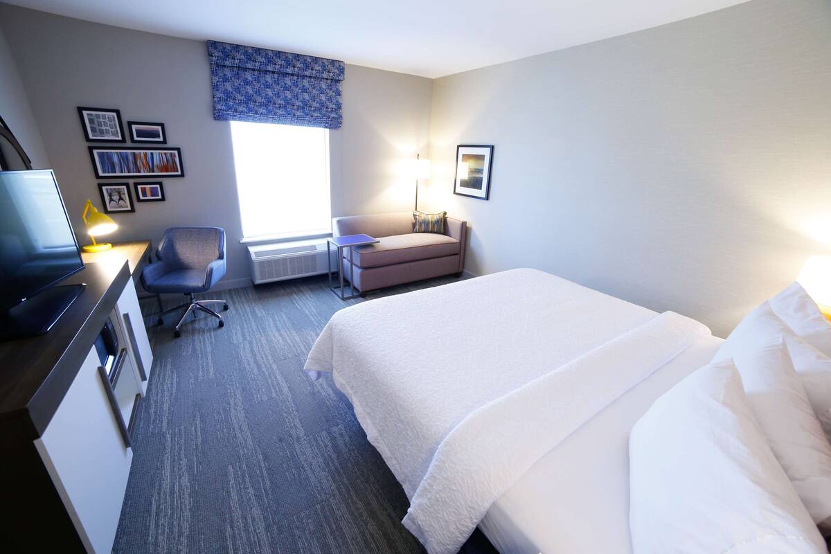 Ein Hotelzimmer mit einem Bett, einem Schreibtisch mit Computer, einem Stuhl, einem kleinen Tisch und einem Fenster mit Blick.