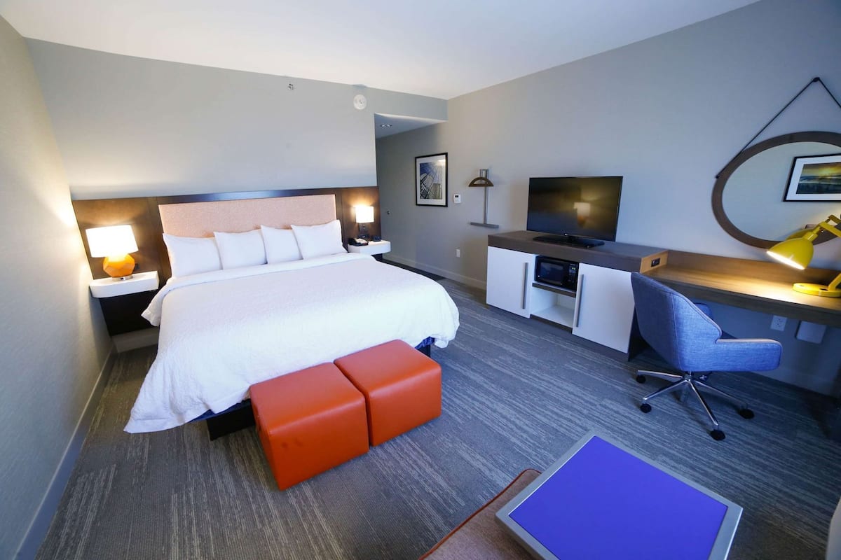 A hotel room with a bed, a desk, a chair, a TV, and a desk lamp.