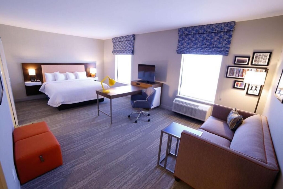 A hotel room with a bed, desk, chair, sofa, and a small table.