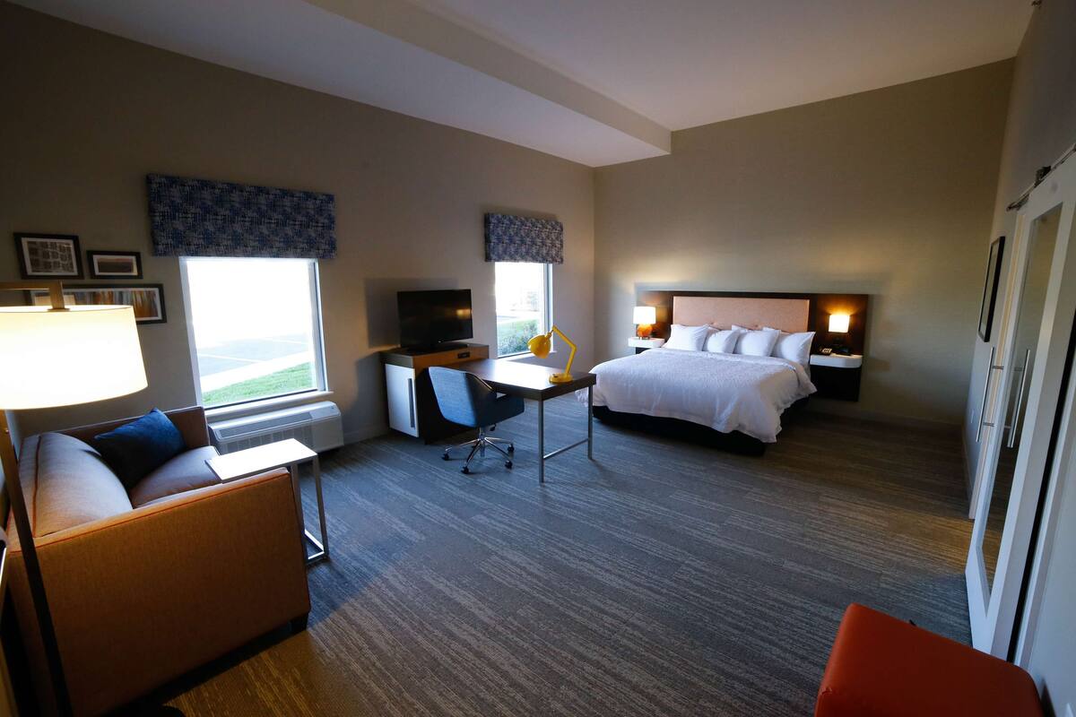 Ein Hotelzimmer mit Bett, Schreibtisch, Stuhl, Sofa und Fernseher.
