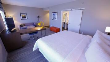 A hotel room with a large bed, a desk with a chair, a sofa, and a TV.