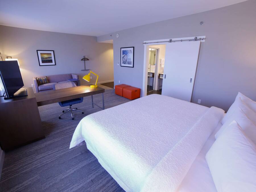 A hotel room with a large bed, a desk with a chair, a sofa, and a TV.