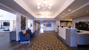 Un hall d’hôtel moderne avec un comptoir d’accueil, un espace détente aux sièges bleus et une moquette à motifs.