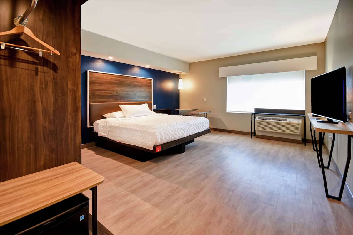 Una habitación de hotel moderna con una cama grande, mesitas de noche, un escritorio, un televisor y una ventana con vistas.
