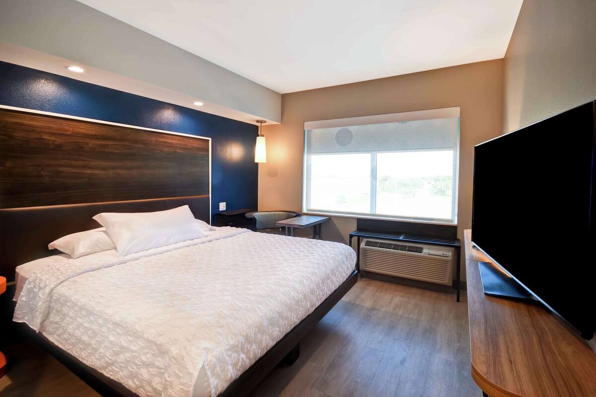 Una habitación de hotel moderna con una cama grande, un escritorio, un televisor de pantalla plana y una ventana con vista a la ciudad.
