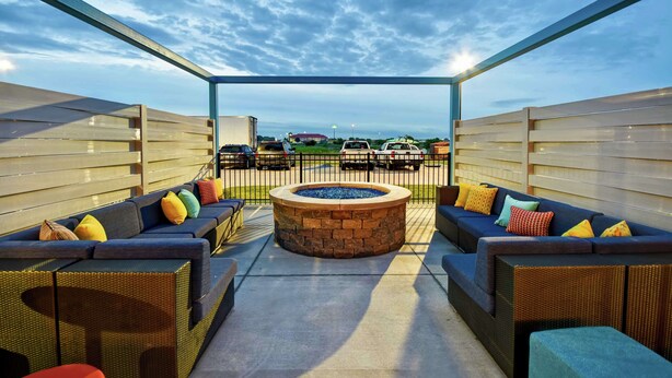An outdoor seating area with two sofas and a fire pit, surrounded by a metal fence.