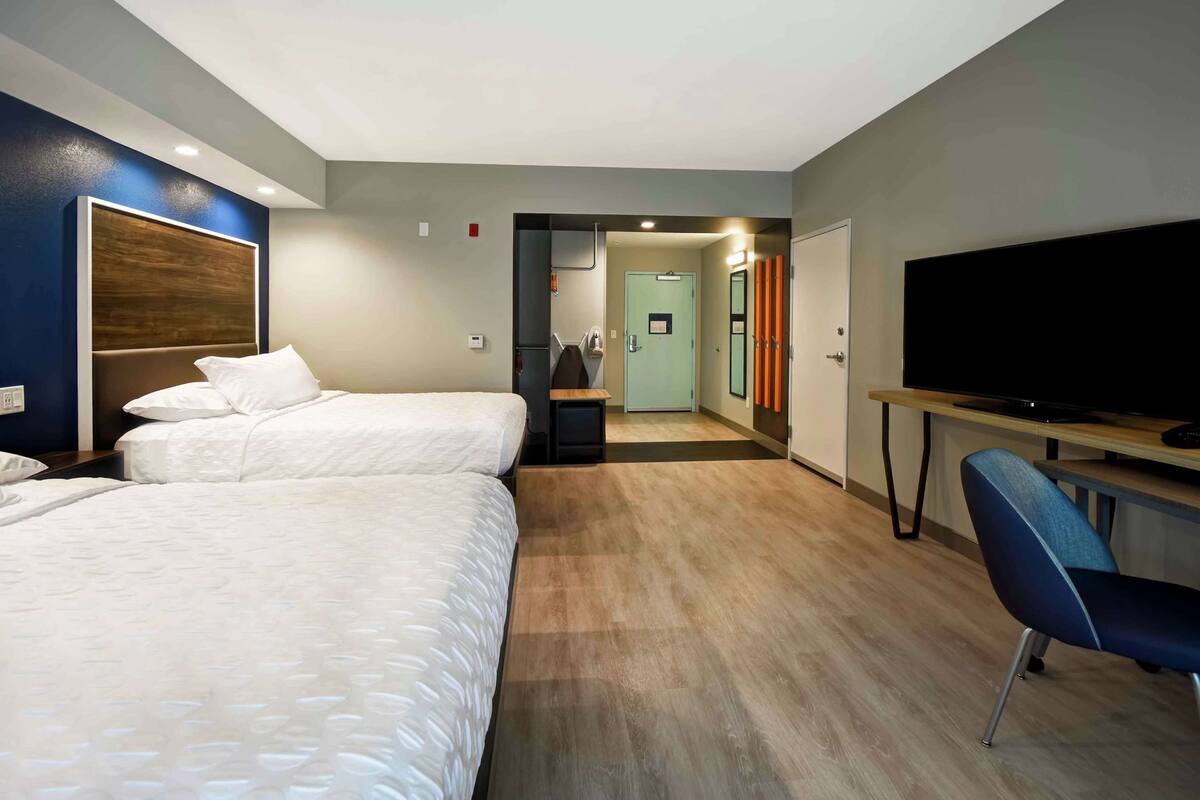 Habitación de hotel con dos camas, un escritorio, televisor de pantalla plana y una silla.