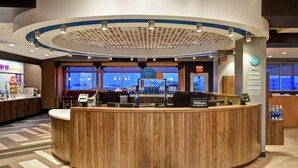 A hotel reception area with a wooden counter, a digital screen, and a view of the cityscape through large windows.