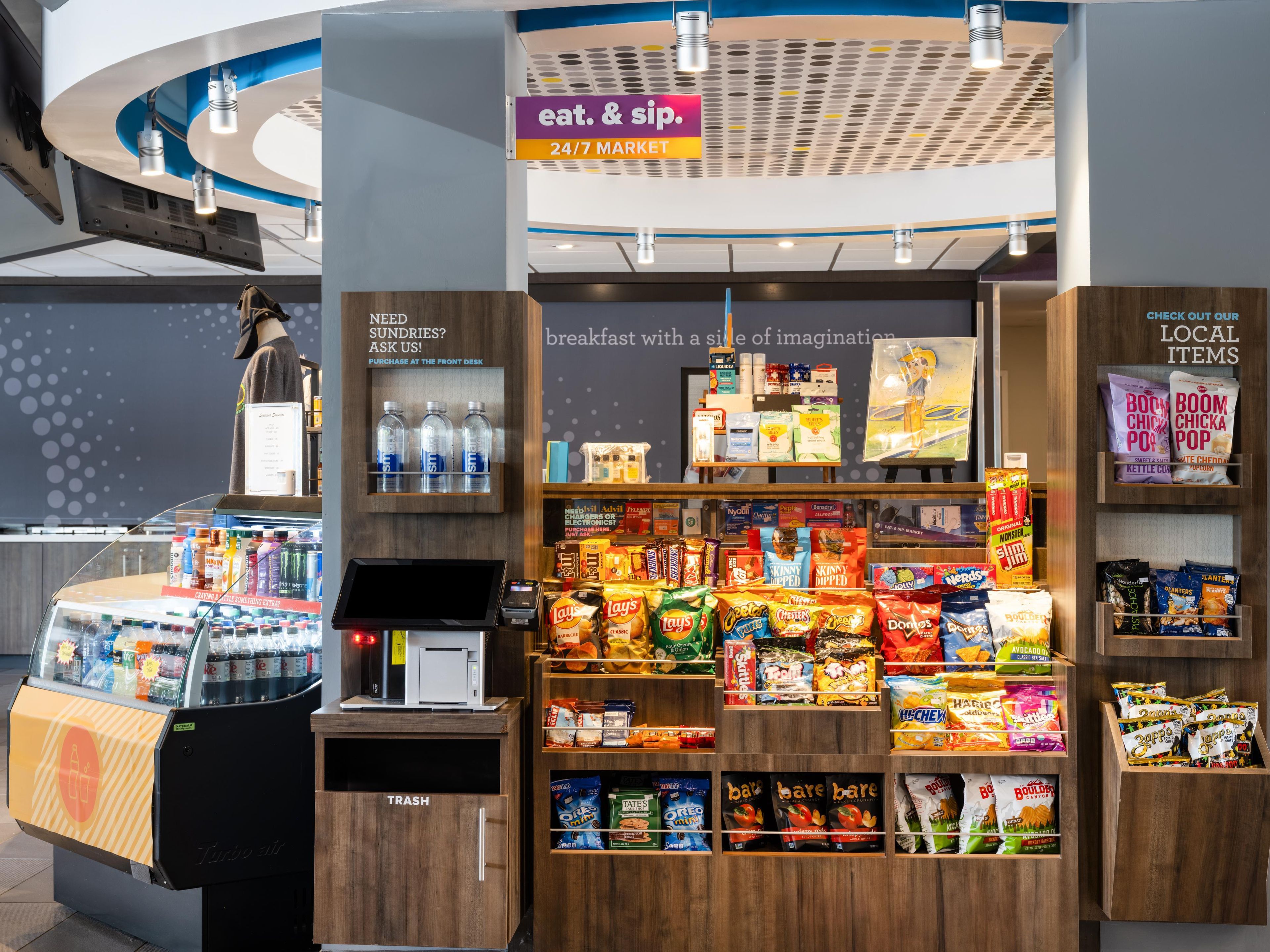 A snack kiosk with a variety of snacks and beverages, a front desk for purchases, and a sign indicating 24/7 market availability.