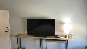 A room with a TV on a wooden desk, a lamp, a phone, and a trash can.