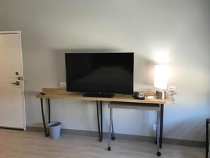 Una habitación con una televisión sobre un escritorio de madera, una lámpara, un teléfono y un cubo de basura.
