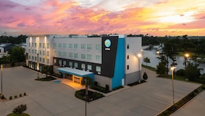 A modern hotel with a prominent logo, a parking lot, and a body of water in the background. - Tru By Hilton Lake Charles (Lake Charles)