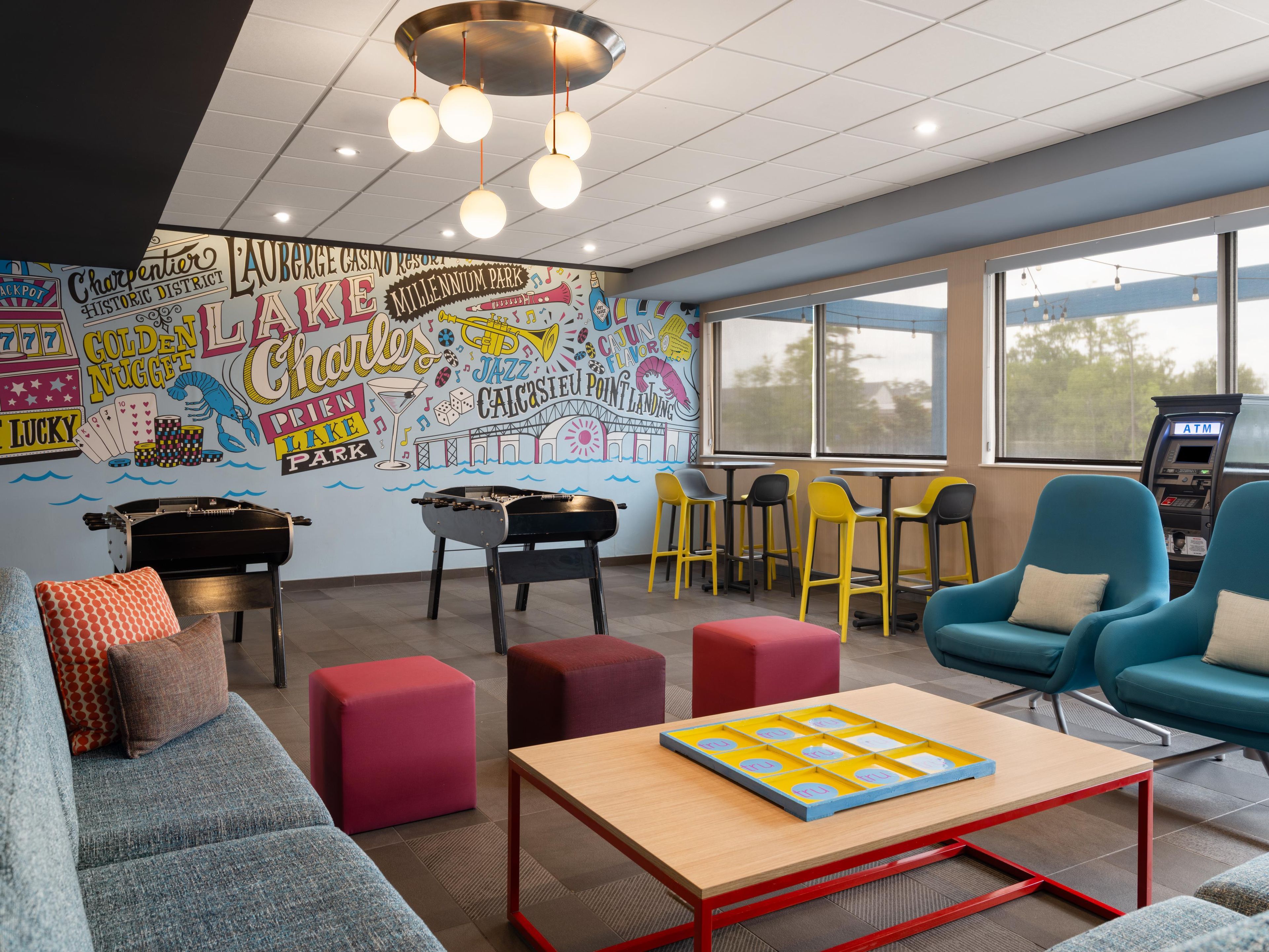 Espaço de convívio com mural, assentos, mesa de pebolim e caixa eletrônico.