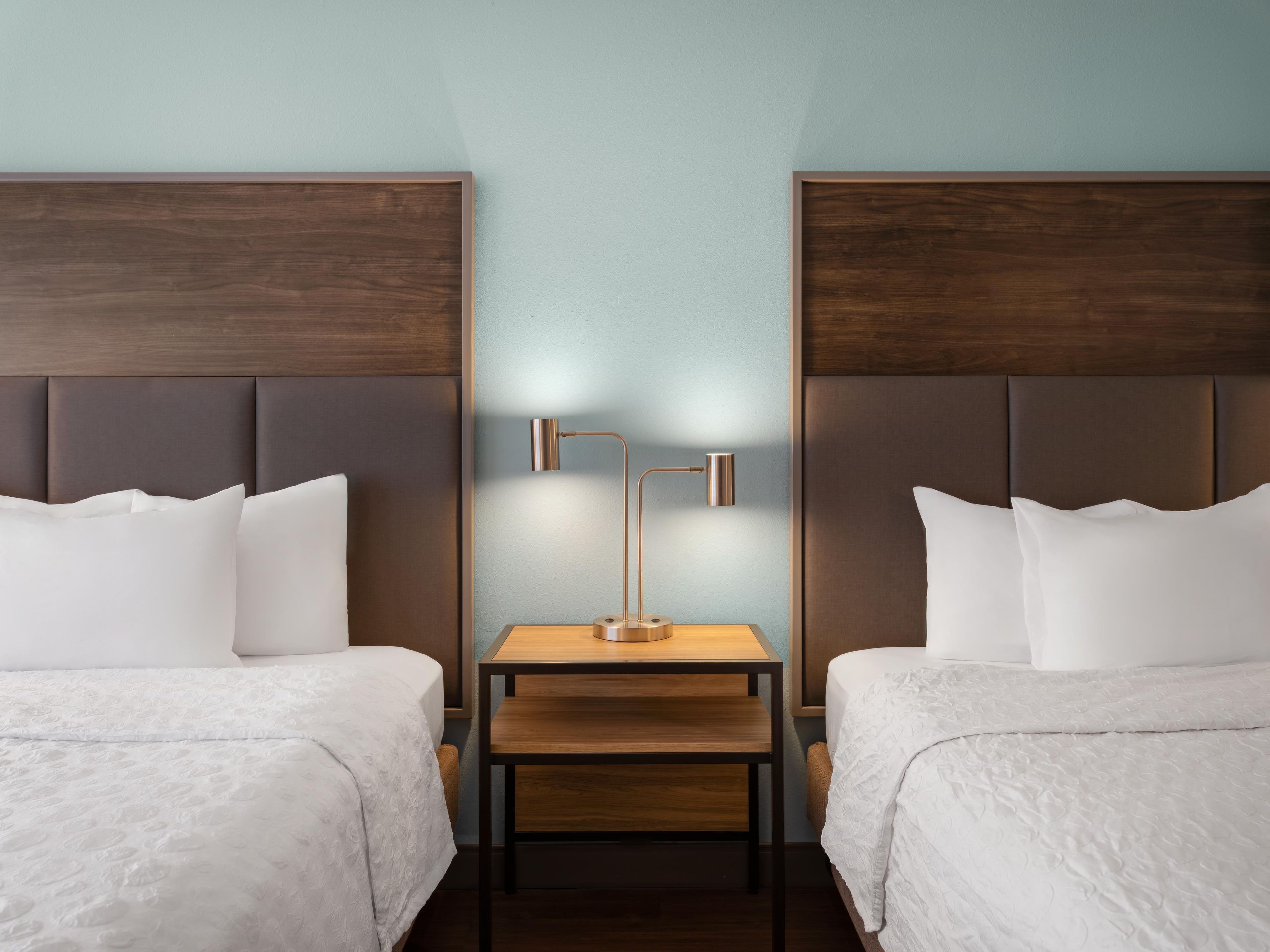 Een hotelkamer met twee bedden, een nachtkastje ertussen en een lamp aan de muur.