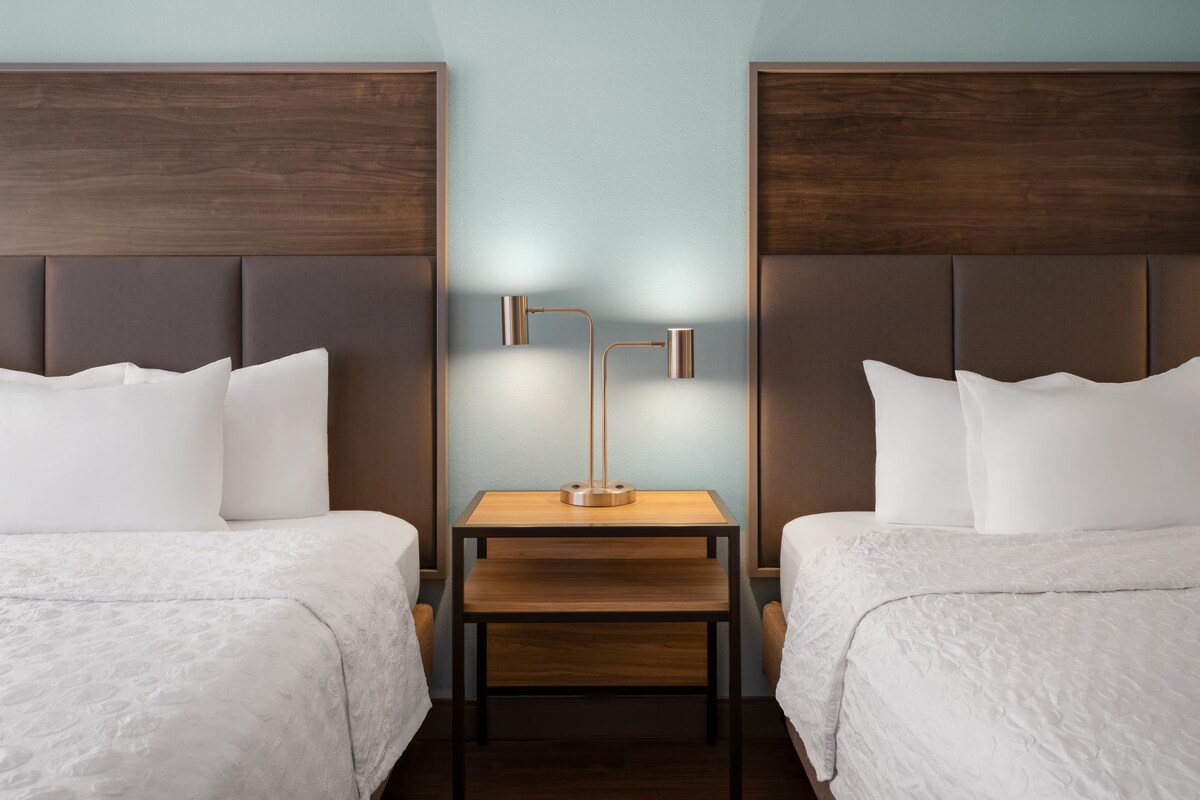 Una habitación de hotel con dos camas, una mesita de noche entre ellas y una lámpara fijada a la pared.