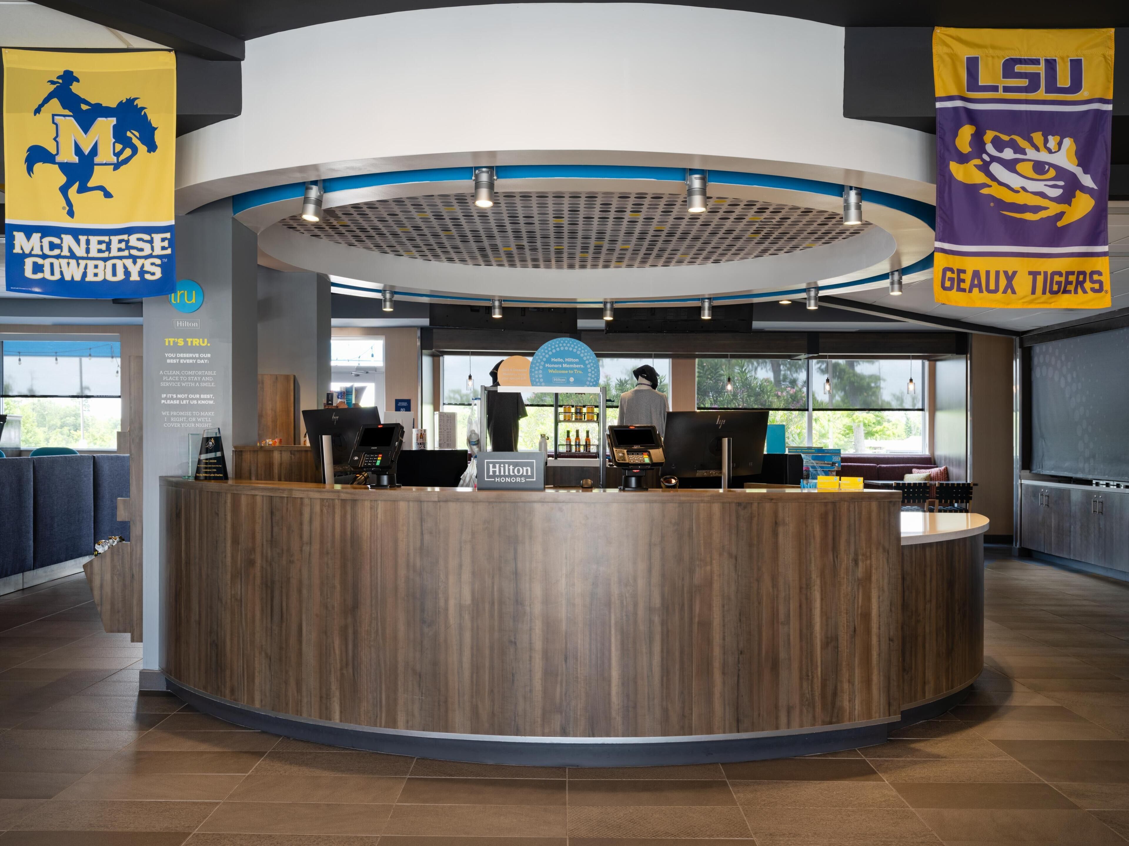 A hotel reception desk with a circular design, a digital kiosk, and a view of the outside.