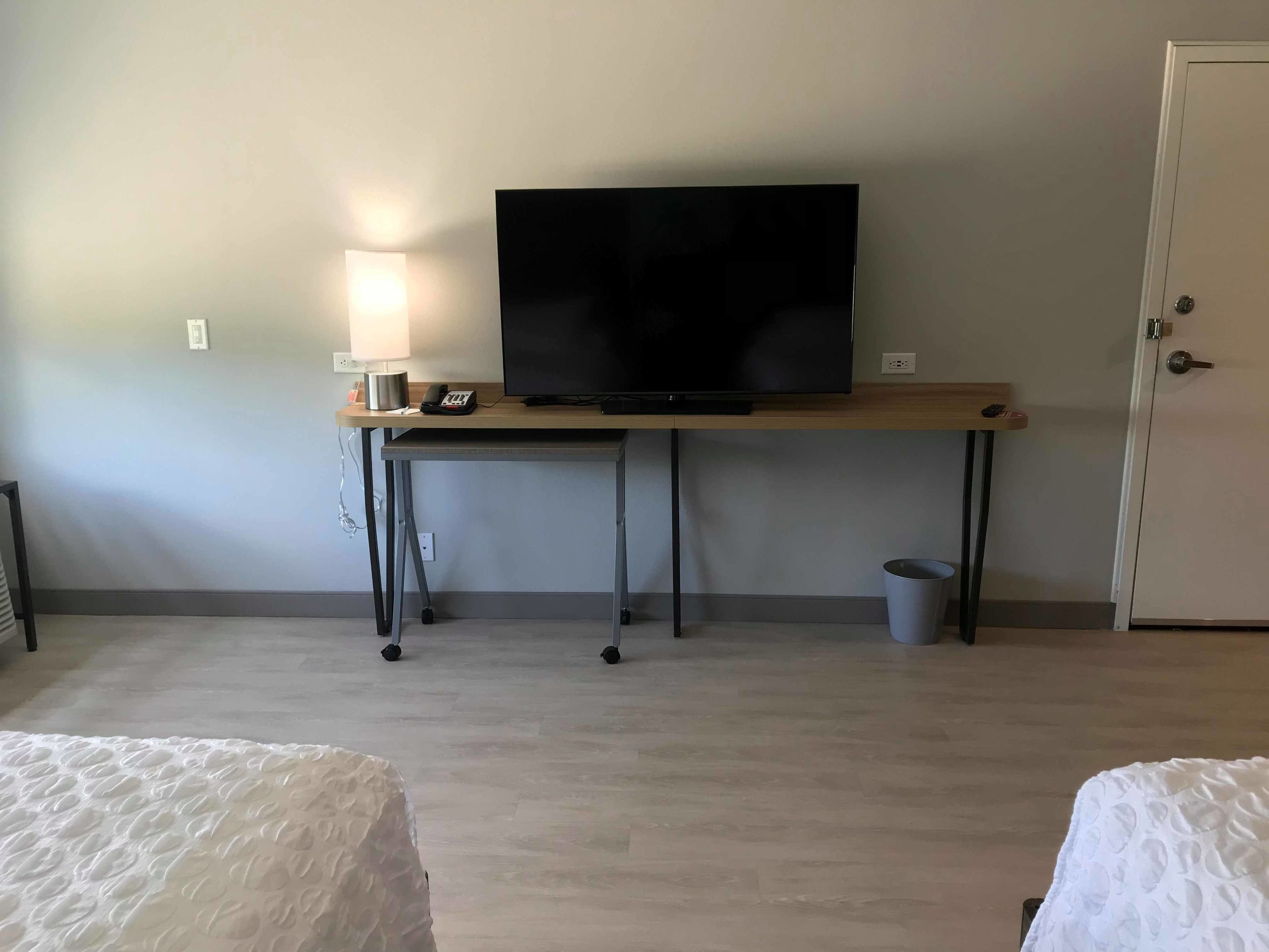 Une chambre d’hôtel avec un bureau en bois, une télévision, une lampe et une porte.