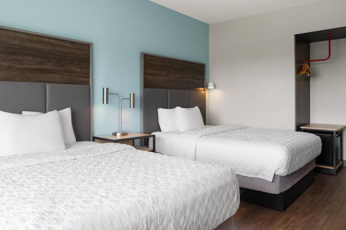 Ein Hotelzimmer mit zwei Betten, einem Nachttisch, einer Lampe und einem Kleiderschrank.