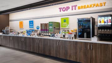 A breakfast counter with a sign reading 'TOP IT BREAKFAST' and various food options like pancakes and yogurt.