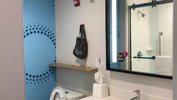 Une salle de bain moderne équipée de toilettes, d’un lavabo et d’une douche. On y trouve également un porte-serviettes, un distributeur de savon et un sèche-mains.