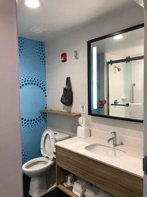 Un baño moderno con inodoro, lavamanos y ducha. Cuenta con un perchero, dispensador de jabón y secamanos.