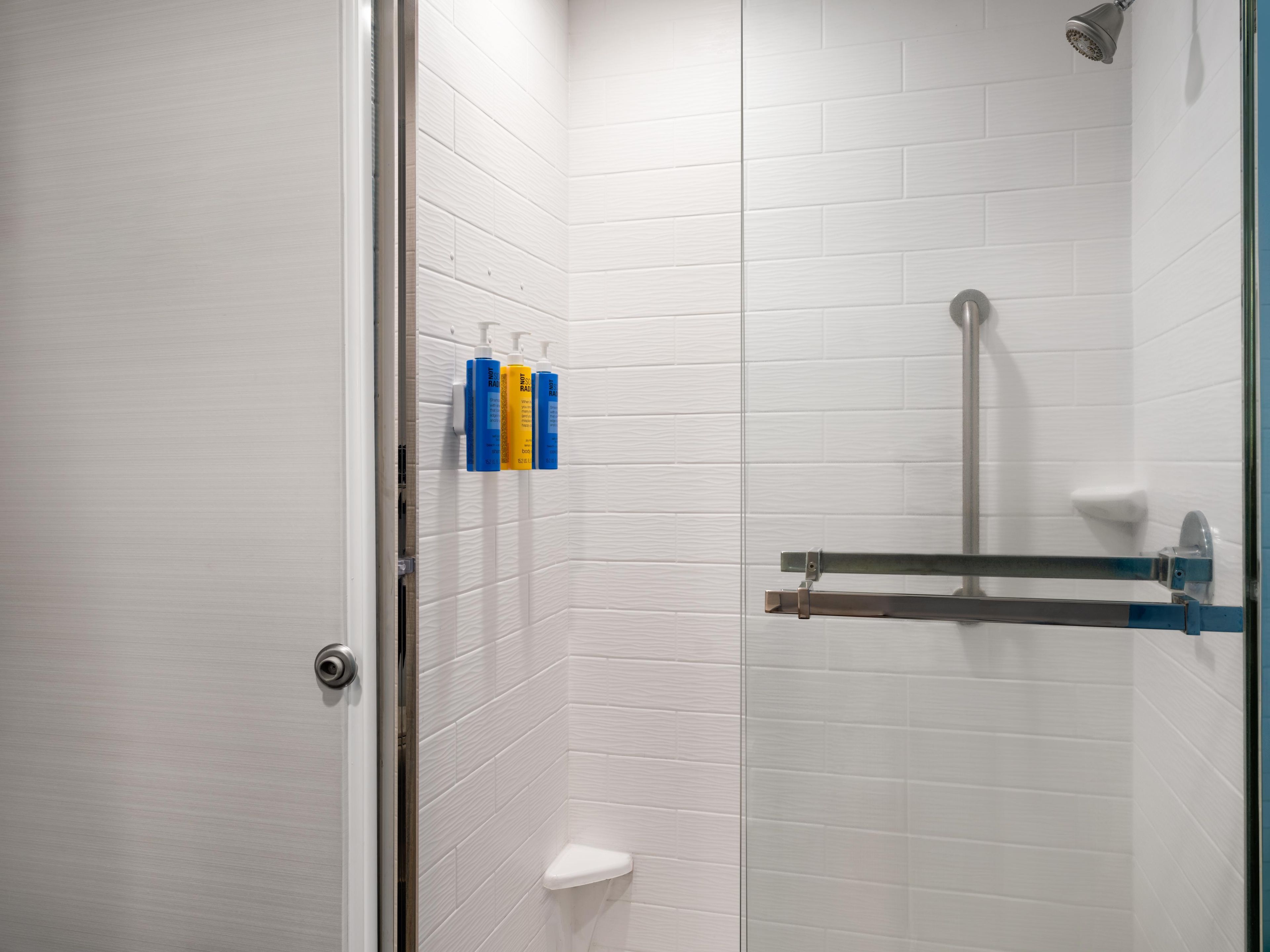 A bathroom with white tiled walls, a glass shower enclosure, a toilet, and a towel rack with bottles.
