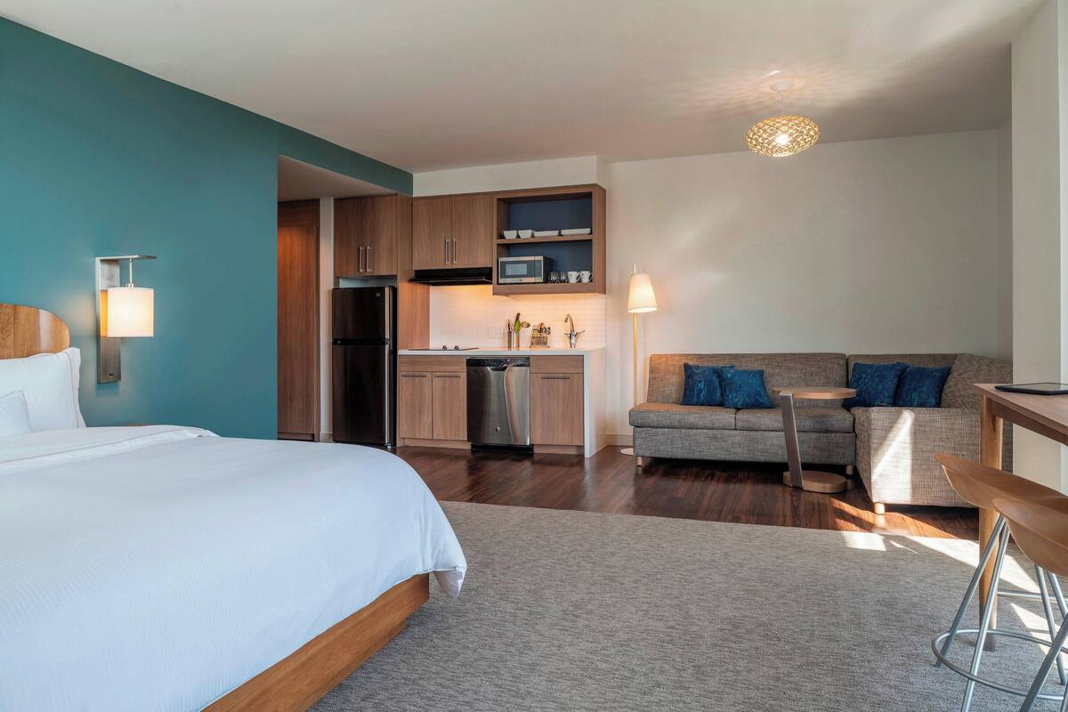 Une chambre d’hôtel moderne comprenant un lit, un canapé, une table à manger, un coin cuisine et une salle de bain.