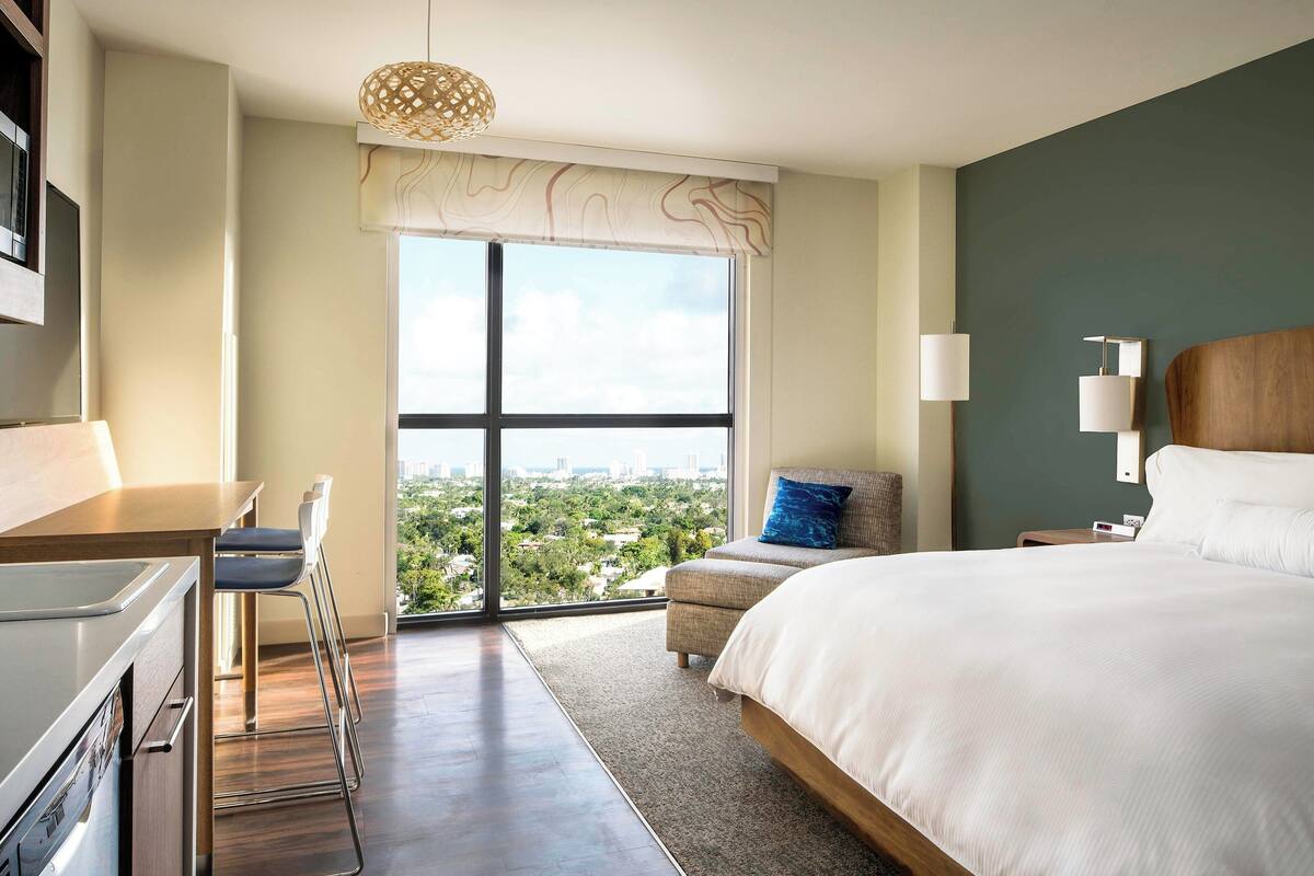 Une chambre d’hôtel moderne, dotée d’un grand lit, d’un bureau et offrant une vue sur la ville grâce à une grande fenêtre.