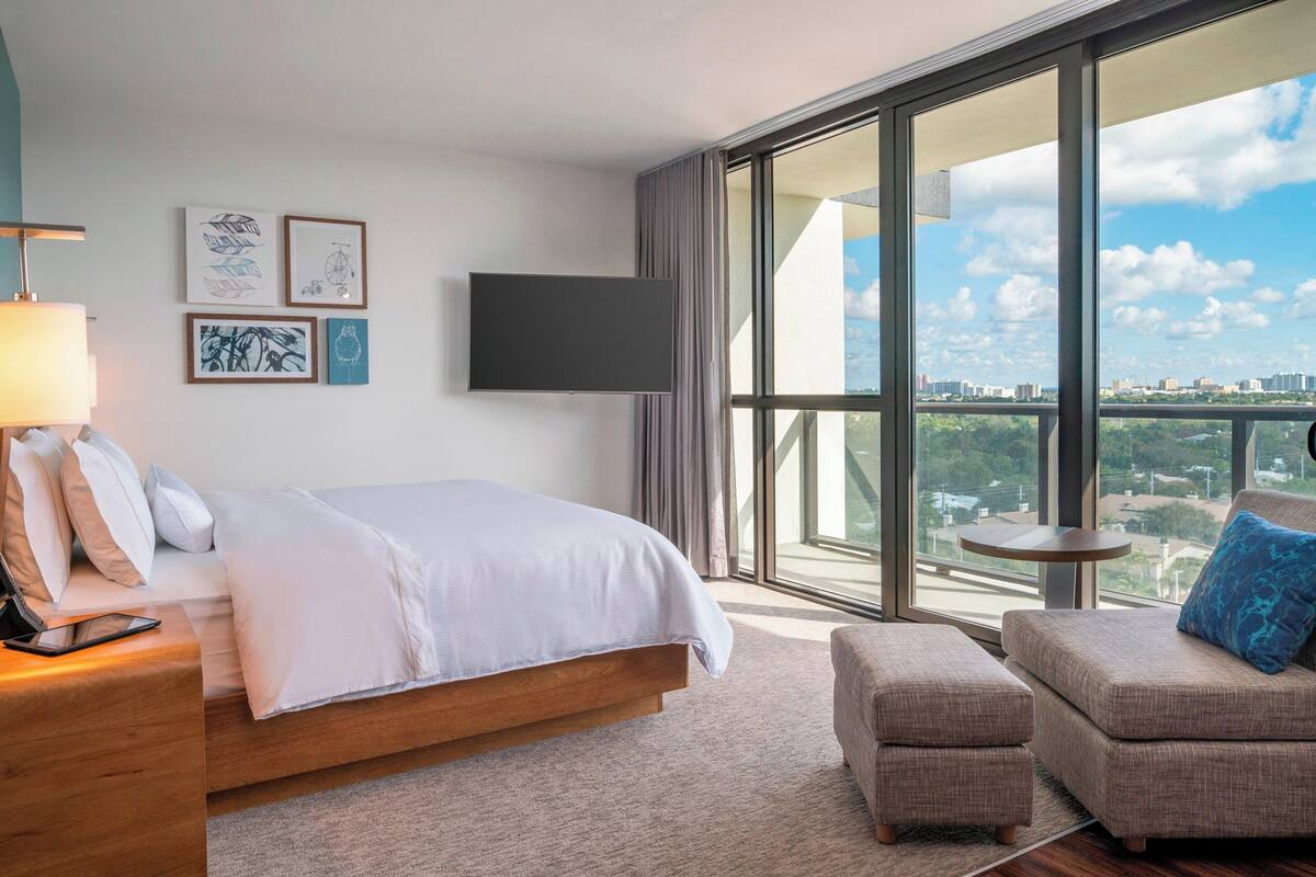 Une chambre d’hôtel moderne dotée d’un grand lit, d’un coin salon, d’une télévision à écran plat et d’un balcon offrant une vue sur la ville.
