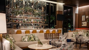 A bar area with shelves of bottles and glasses, a seating area with sofas and chairs, and a large window with curtains. - Element by Marriott Fort Lauderdale Downtown (Fort Lauderdale)