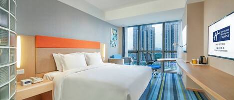 A hotel room with a bed, bedside table, lamp, and a view of the city.