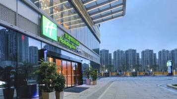 Edifici de Holiday Inn Express amb façana de vidre moderna, envoltat d'edificis alts i plantes en testos al primer pla.