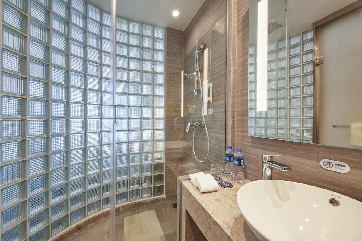 A modern bathroom with a glass shower enclosure, a sink with a mirror, and toiletries on the counter.