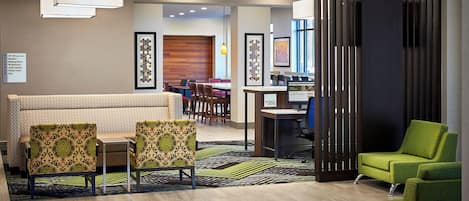 A hotel lobby with a reception desk, a seating area with patterned chairs, a green armchair, and a wooden partition.