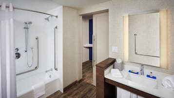 A bathroom with a bathtub, shower, and sink, featuring a patterned wall and wooden flooring.