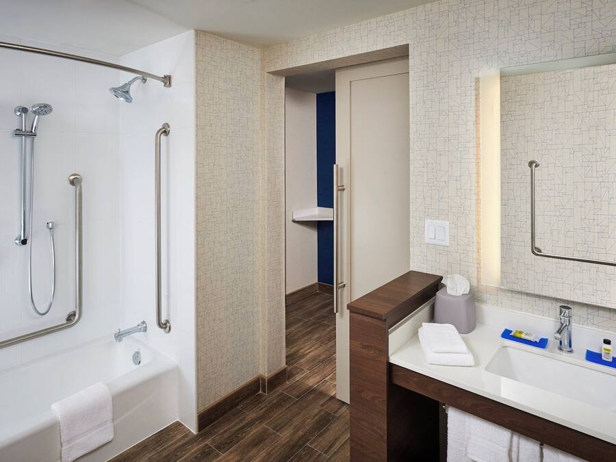A bathroom with a bathtub, shower, and sink, featuring a patterned wall and wooden flooring.